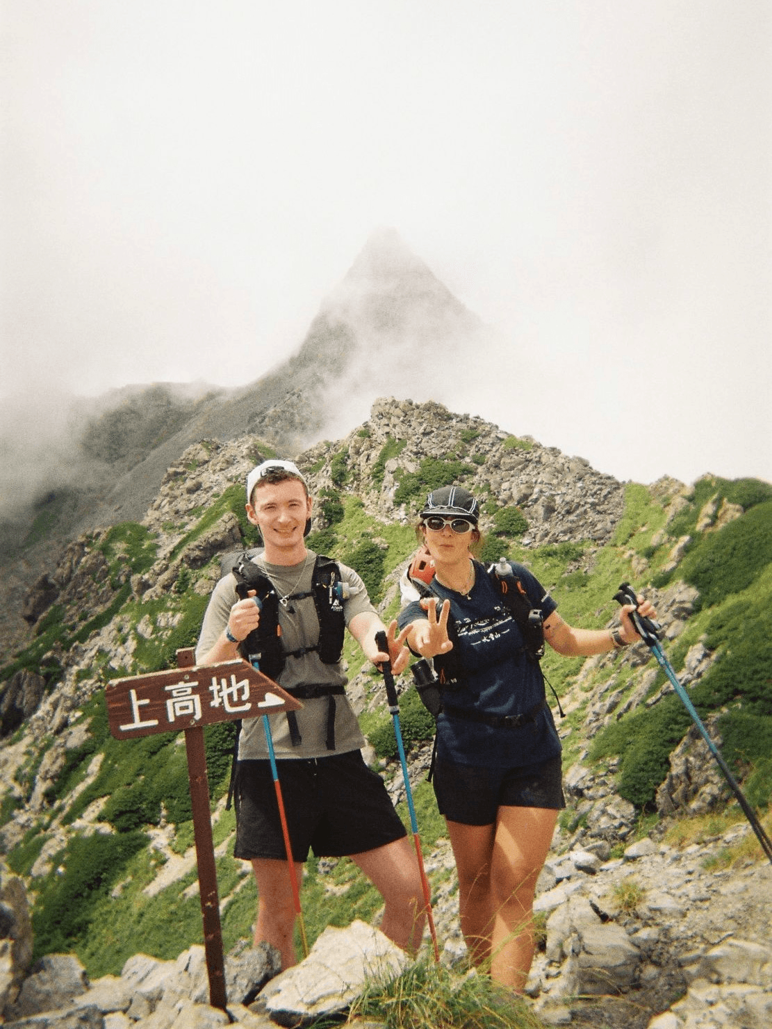 Two hikers at a mountain summit sign