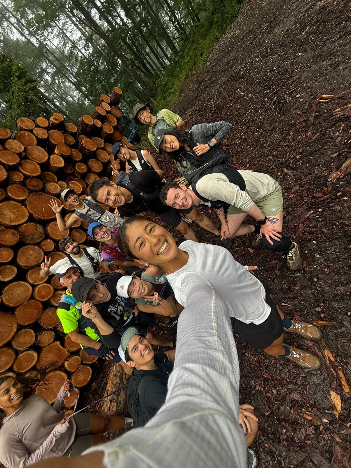 Group selfie on a trail run beside a stack of logs